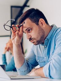 Man removing glasses while looking at laptop