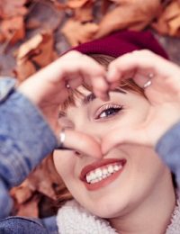 Smiling woman through heart-shaped fingers