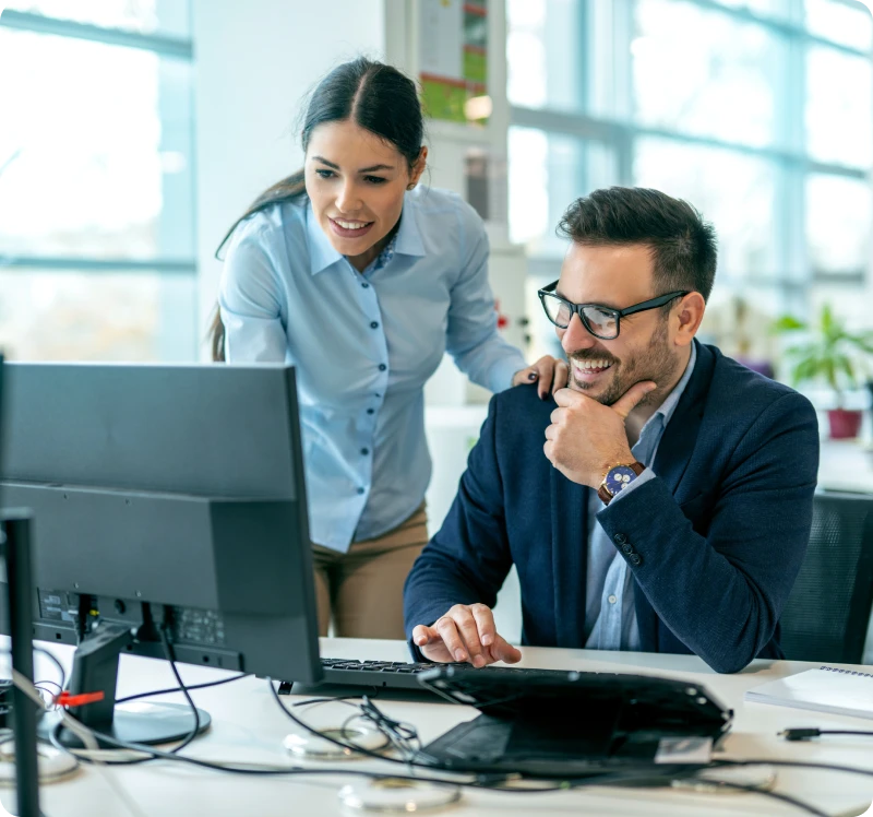 Smiling coworkers reviewing work on monitor