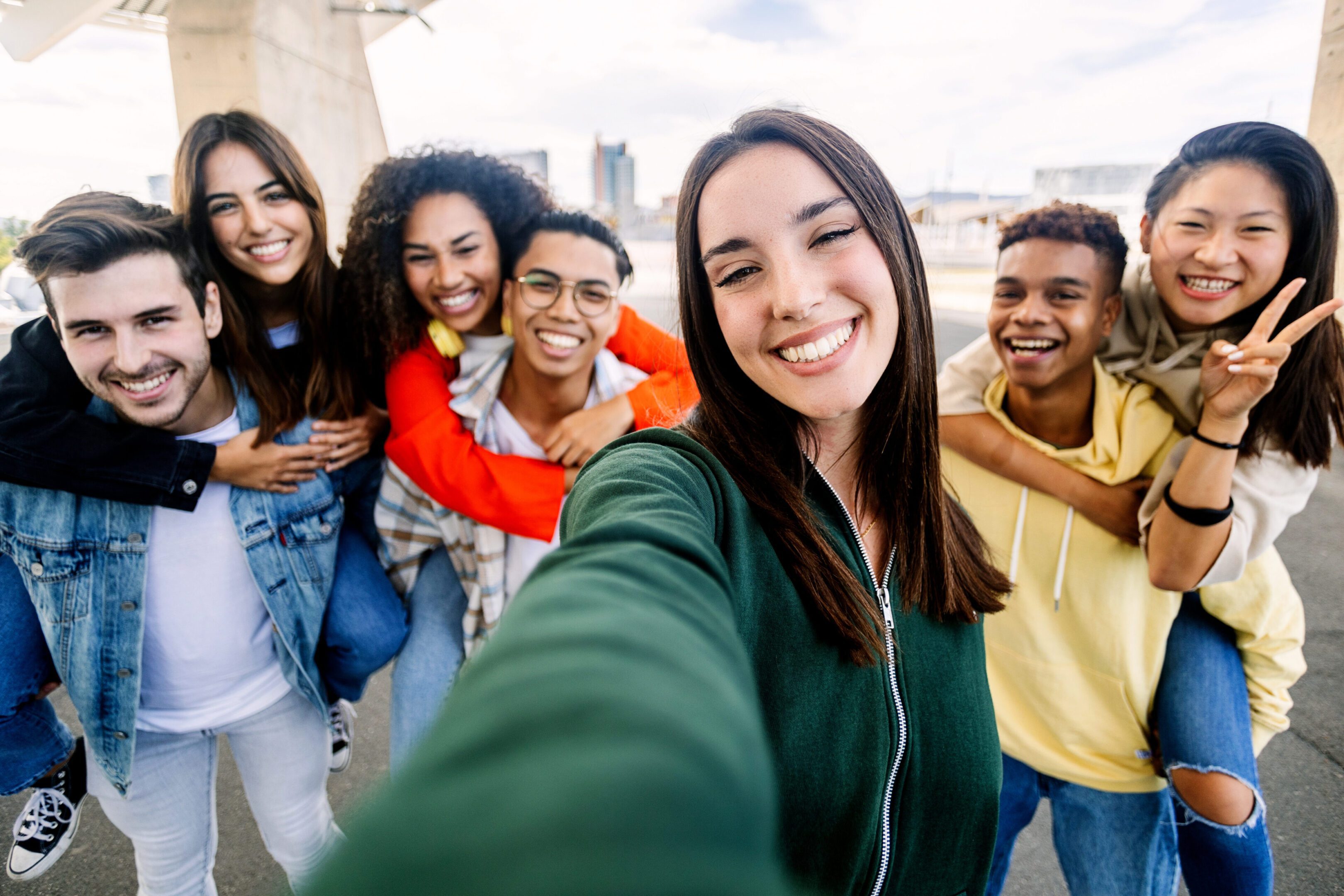 Young group of diverse students having fun together outdoors. Beautiful woman smile at camera taking selfie portrait with diverse friends on the background. Youth community concept.