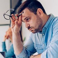 Man removing glasses while looking at laptop