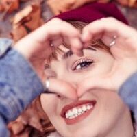 Smiling woman through heart-shaped fingers